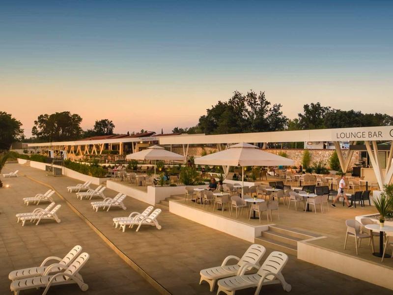 Playa con tumbonas blancas y sombrillas frente a un hotel al atardecer.