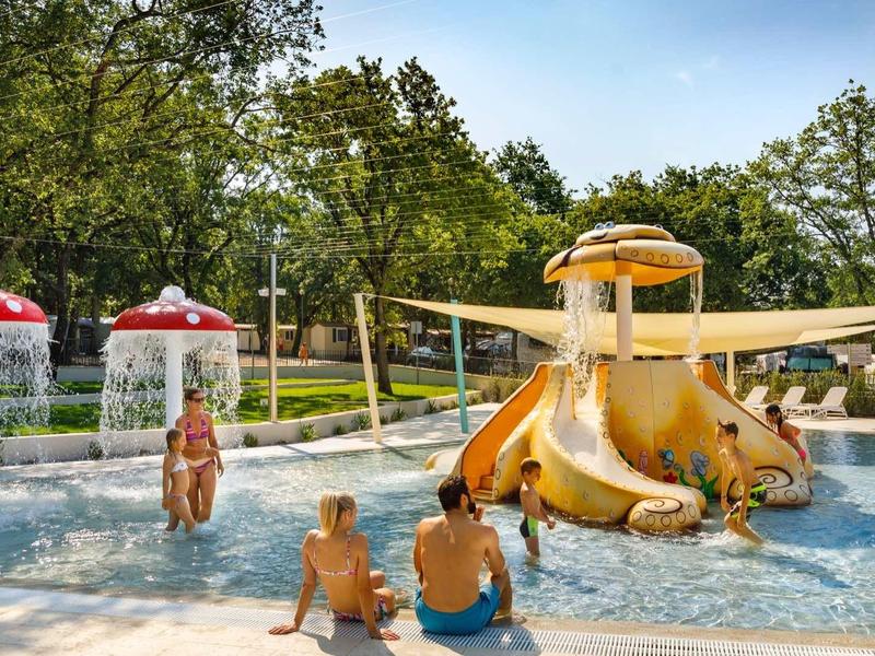 Niños juegan en un área de agua poco profunda con toboganes y juegos de agua al aire libre.