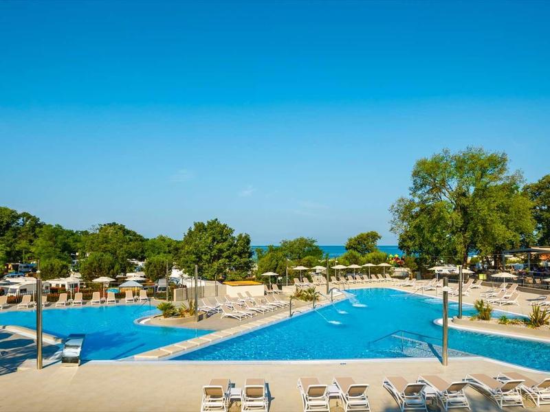 Gran piscina exterior con tumbonas y áreas verdes bajo un cielo azul despejado.