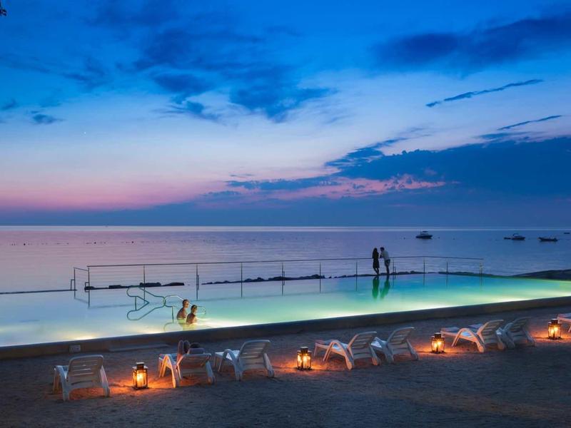 Piscina infinita iluminada al atardecer con vista al mar en la playa.