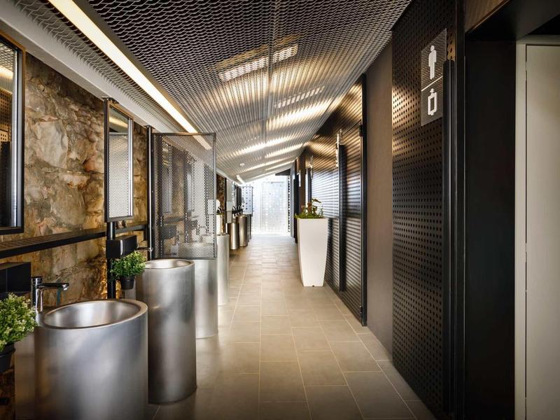 Pasillo moderno de hotel con puertas negras, plantas grandes y luces de techo brillantes.