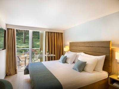 Chambre d'hôtel lumineuse avec grand lit, décoration moderne et balcon donnant sur la nature verte.