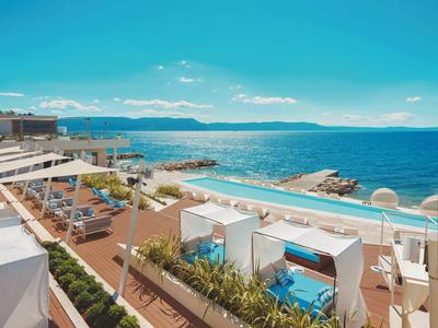 Terrasse de luxe avec piscine, espaces lounge et vue sur la mer sous un ciel dégagé.