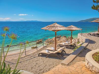 Plage avec chaises longues et parasols au bord d'une mer bleue claire sous un ciel bleu.