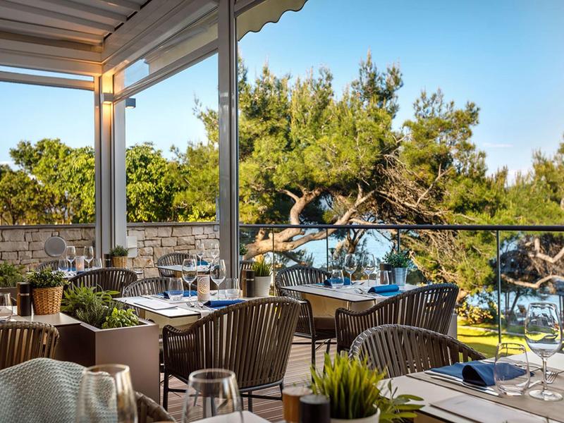 Terrasse d'hôtel avec vue sur la mer, tables dressées et chaises sous un auvent.