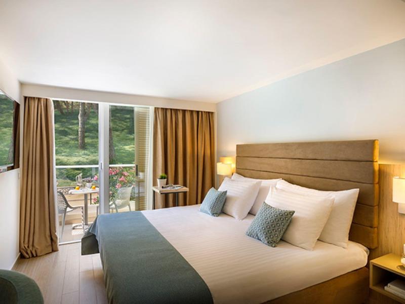 Chambre d'hôtel lumineuse avec grand lit, décoration moderne et balcon donnant sur la nature verte.