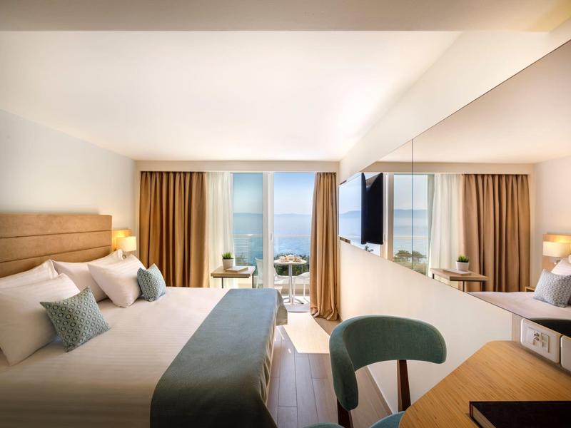 Chambre d'hôtel moderne avec deux lits, grand miroir et balcon avec vue sur la mer.