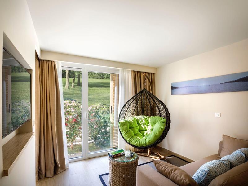 Salon lumineux avec fauteuil suspendu vert, canapé et vue sur le jardin par de grandes fenêtres.