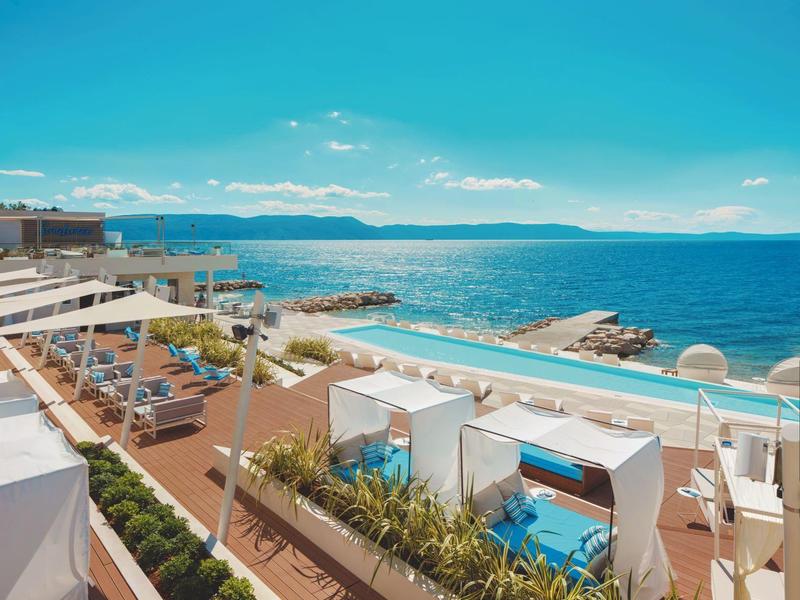 Terrasse de luxe avec piscine, espaces lounge et vue sur la mer sous un ciel dégagé.