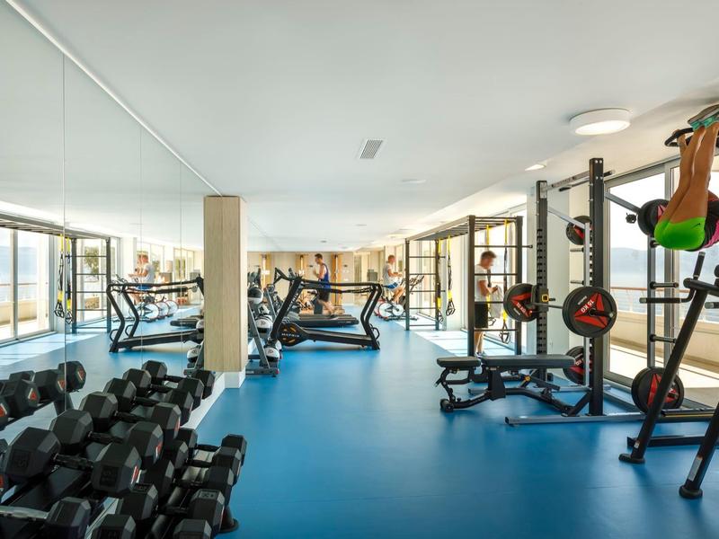 Salle de sport moderne avec haltères, tapis de course et machines de musculation, lumière naturelle abondante.