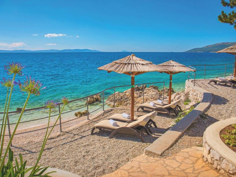 Plage avec chaises longues et parasols au bord d'une mer bleue claire sous un ciel bleu.