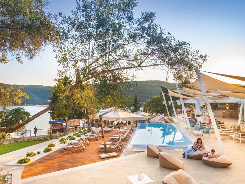 Espace piscine extérieur moderne avec transats, parasols et vue sur la montagne au coucher du soleil.