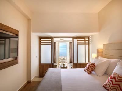 Habitación de hotel luminosa con cama grande y balcón con vista al mar.