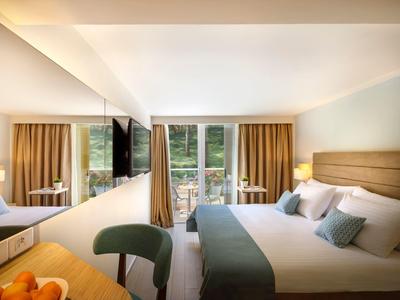 Habitación de hotel moderna con cama doble, balcón y vista a áreas verdes.