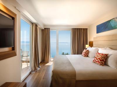 Habitación de hotel moderna con vista al mar, cama grande y acceso al balcón con área de descanso.