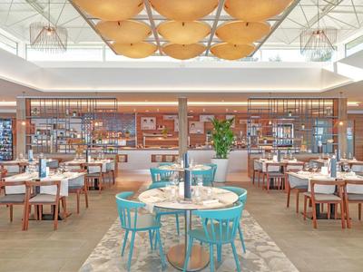 Licht, modern restaurant met blauwe en witte stoelen en een ruime, luchtige ruimte.