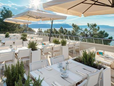 Terras van een restaurant met witte tafels en stoelen bij de zee onder een zonnige hemel.