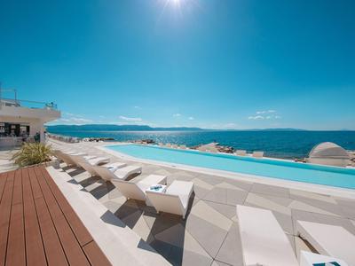 Infinity zwembad met witte ligbedden en uitzicht op zee onder een heldere lucht.