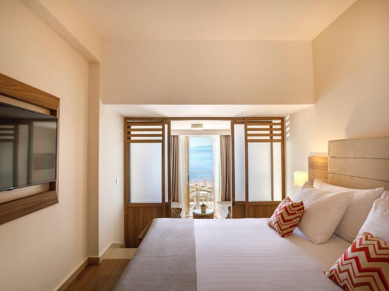 Habitación de hotel luminosa con cama grande y balcón con vista al mar.