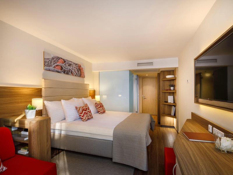 Habitación de hotel moderna con cama doble, muebles de madera y luz cálida.