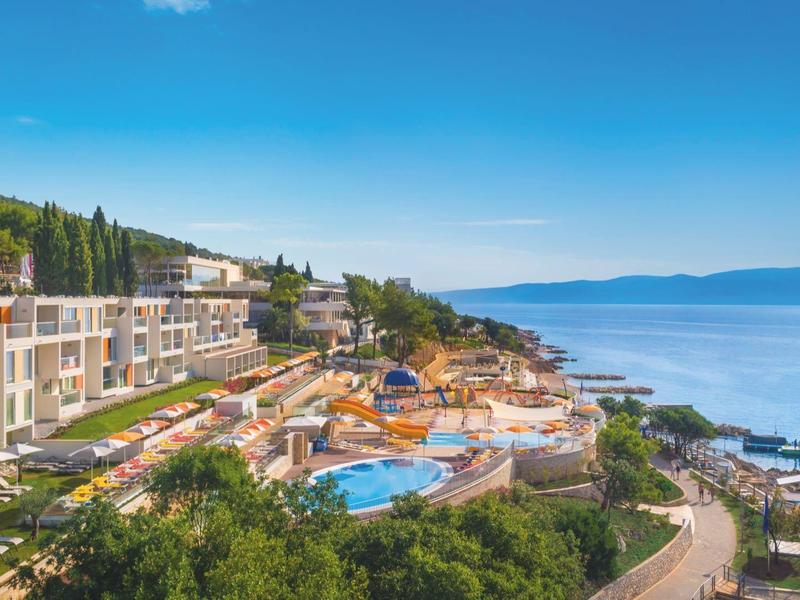Resort hotelero con piscinas y tumbonas en la costa con vista al mar azul y al cielo.