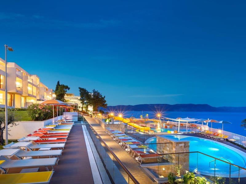 Terraza del hotel al atardecer con piscina iluminada y vistas al mar bajo un cielo despejado.