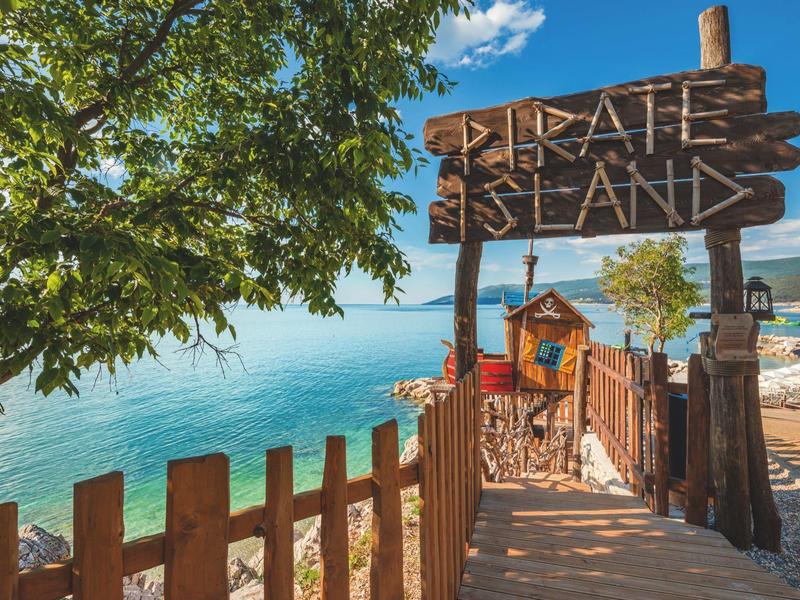 Entrada a isla pirata con cartel de madera y vista al mar azul bajo cielo soleado