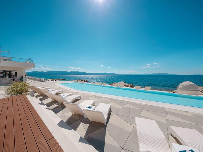 Piscina infinita con tumbonas y vista al mar bajo cielo despejado.