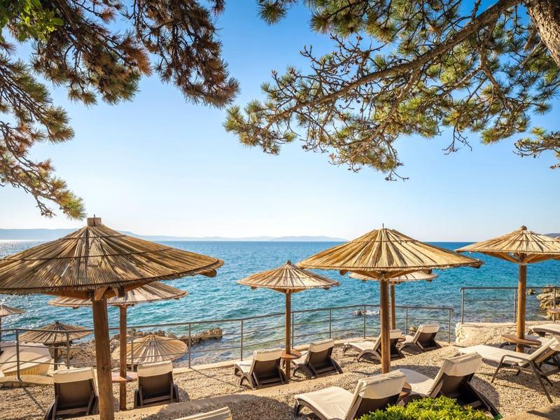 Playa con sombrillas de paja, tumbonas y vista al mar azul y al cielo.
