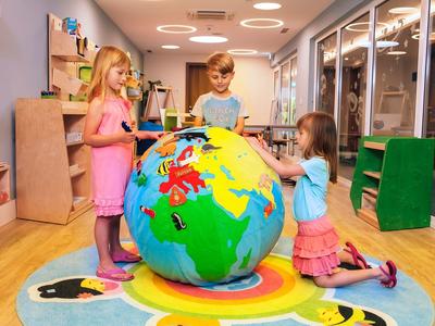 Tres niños juegan con un globo inflable grande en una habitación luminosa con paredes de vidrio.