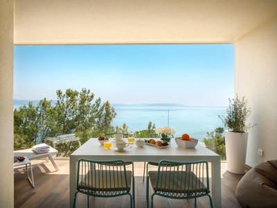Terraza con área de comedor y vista al mar, rodeada de plantas y cielo soleado.