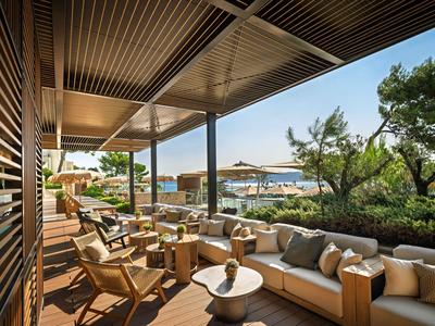 Gezellig terras met bank, stoelen en uitzicht op zee en bomen bij zonnig weer.