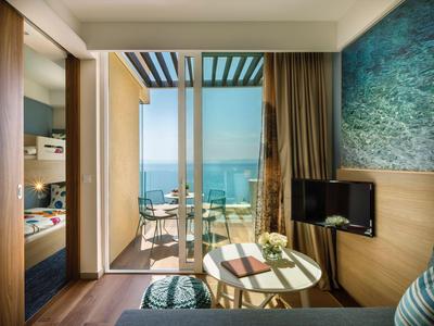 Habitación de hotel moderna con balcón, vista al mar y área de descanso con mesa.