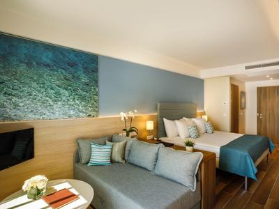 Habitación de hotel acogedora con cama doble, sofá y gran imagen mural del mar.