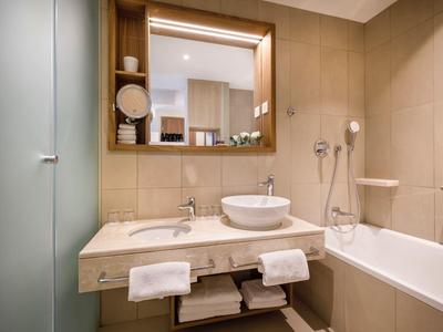 Baño de hotel moderno con espejo grande, lavabo y bañera en tonos beige.