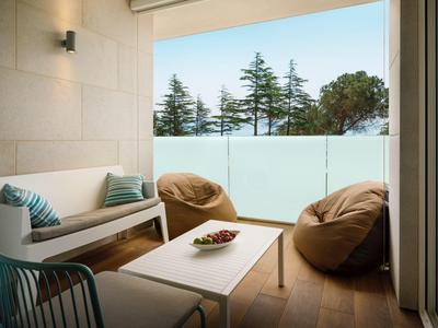 Balcón acogedor con muebles, cojines y vista a árboles detrás de barandilla de vidrio esmerilado.