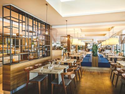 Nowocześnie urządzona restauracja z drewnianymi meblami i dużymi oknami, jasna i przytulna.