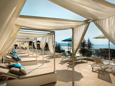 Luksusowe leżaki pod białymi zasłonami z widokiem na morze w słoneczny dzień.