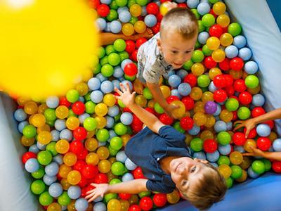 Niños jugando en una piscina de bolas con pelotas de colores en un área de juegos interior.