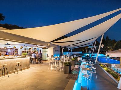 Bar moderno junto a piscina con iluminación azul y toldos blancos bajo cielo nocturno