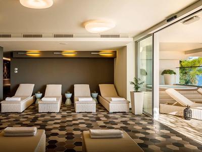 Sala moderna de hotel con tumbonas y grandes ventanales hacia la piscina, luminosa y acogedora.