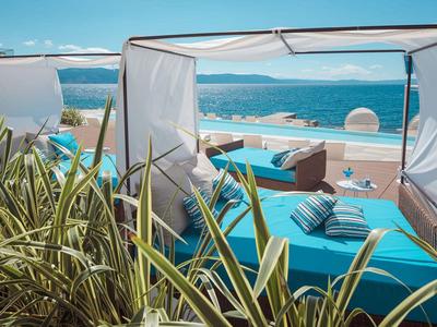 Widok na basen z leżakami pod białym daszkiem i widokiem na morze w tle.