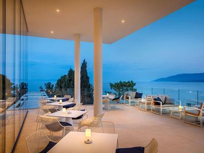 Terraza abierta con mesas y sillas blancas con vistas al mar al atardecer.