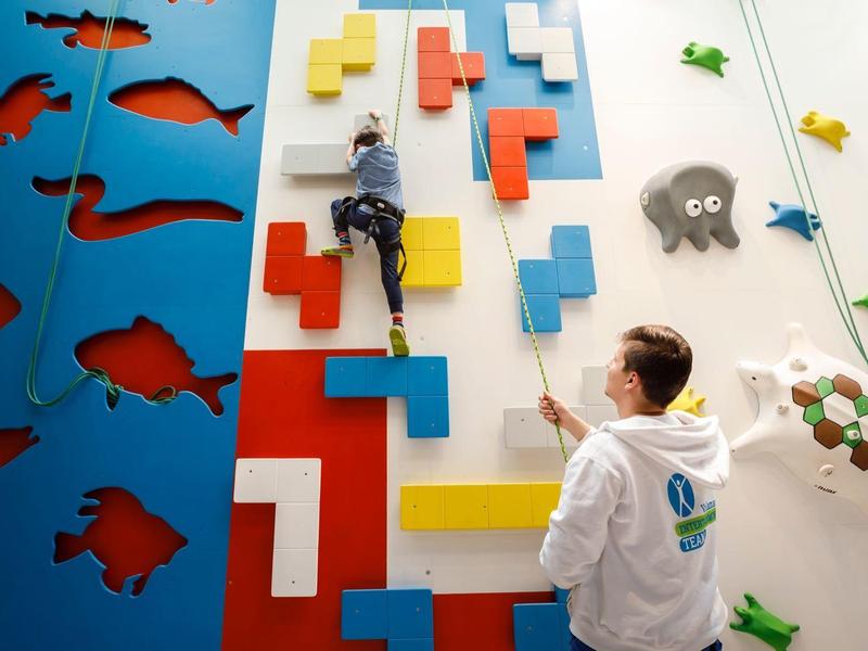 Personas escalan paredes de escalada interiores coloridas en un moderno centro recreativo iluminado.