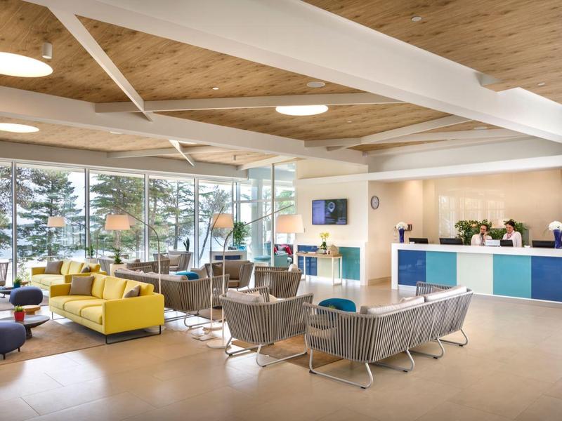 Área de lounge de hotel moderna y luminosa con grandes ventanas y muebles de colores variados.