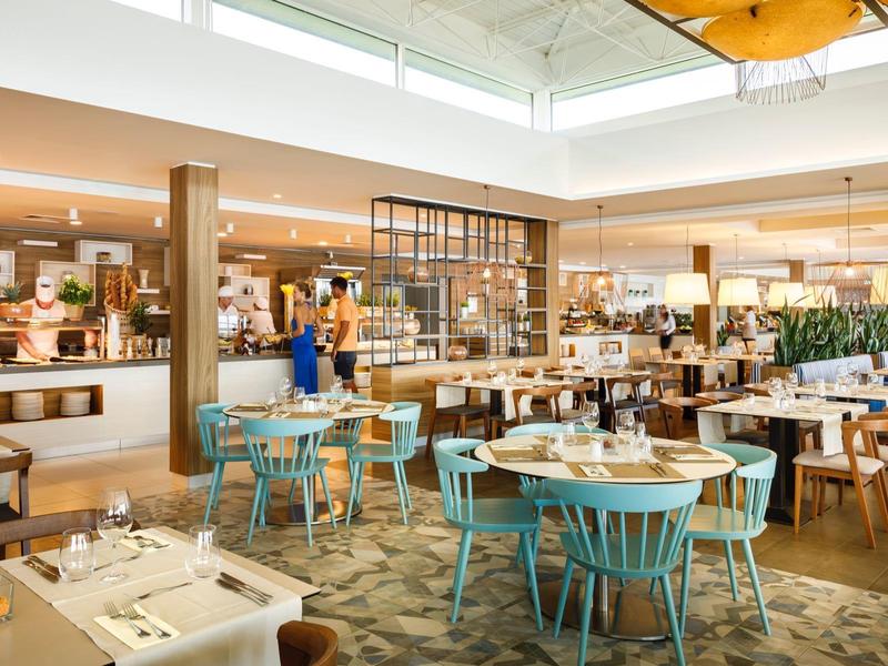 Comedor moderno y luminoso con mesas de madera y sillas azules, luz natural por tragaluces.