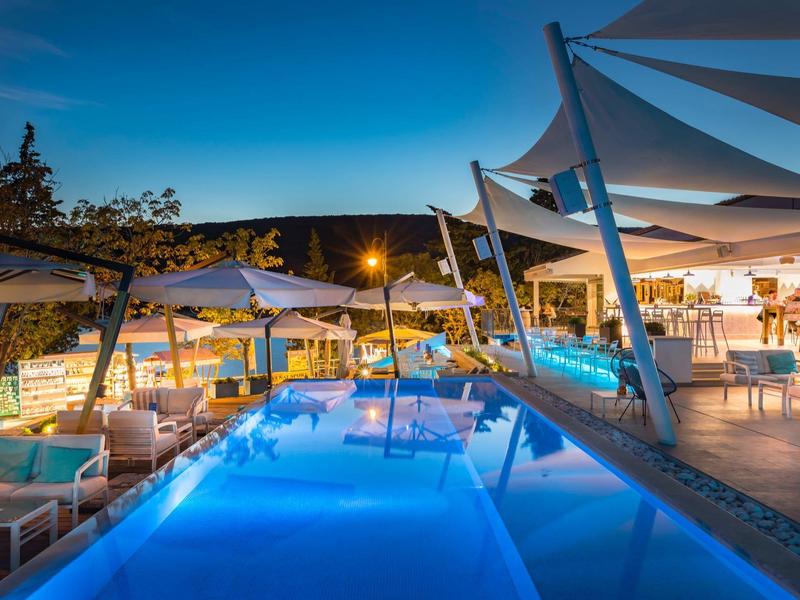 Zona de piscina iluminada con asientos y sombrillas al atardecer.