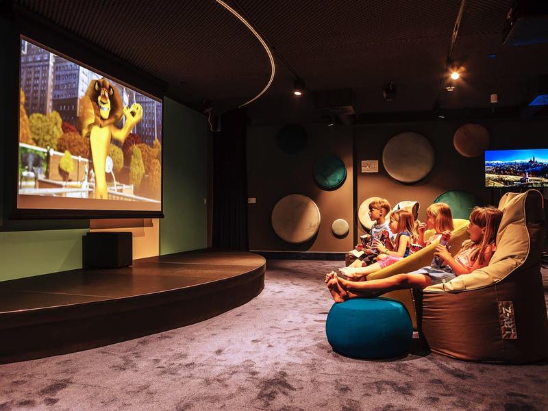 Sala de cine acogedora con cómodos pufs y película animada en pantalla grande.