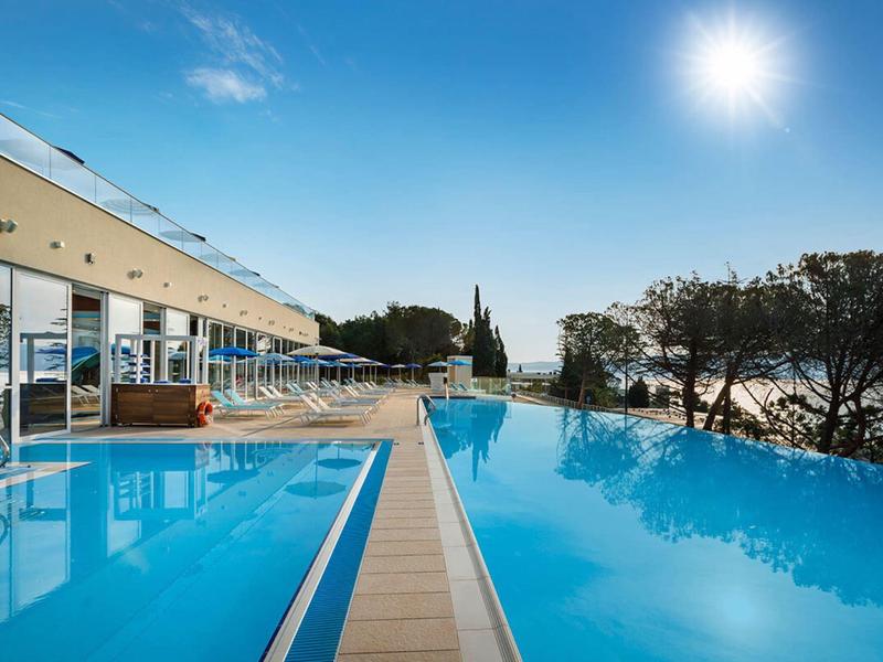 Piscina infinita con vista al mar y luz solar en un complejo hotelero.