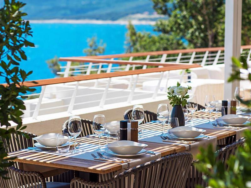 Mesa bien puesta en una terraza con vistas al mar azul y plantas verdes.